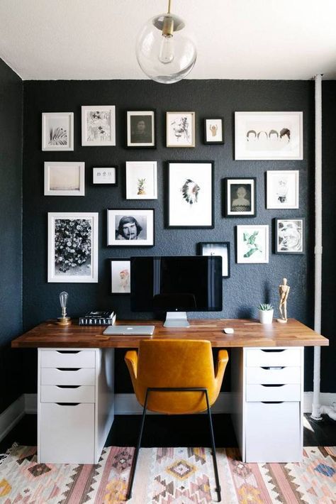 Oficina en casa con pared negra y collage de marcos, escritorio de madera y silla mostaza.