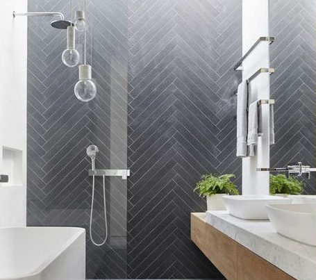 Baño moderno con ducha empotrada, azulejos en zigzag oscuros y lavabo sobre bancada de madera.
